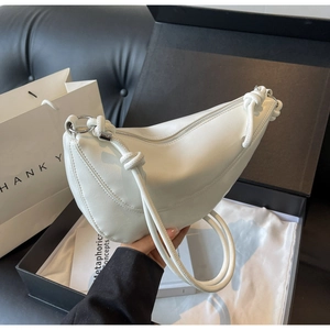 Detailed side view of white crescent bag with knotted strap detail in a luxury gift box