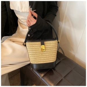 Detail of straw woven bucket bag featuring black leather trim and gold twist lock closure