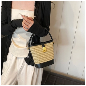 Detailed close-up of woven straw bucket bag featuring black leather trim and golden metal lock