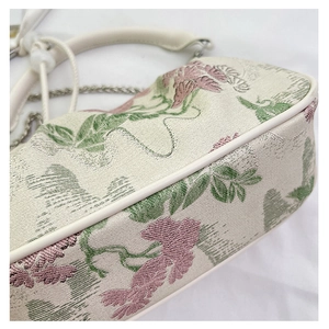 Detailed close-up of floral embroidery on off-white fabric with white leather trim and chain