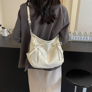Cream patent leather bucket bag with bow accents shown in a stylish commuting scene