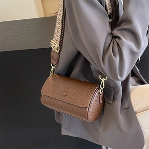 Brown leather cylinder crossbody bag with textured finish and patterned wide strap