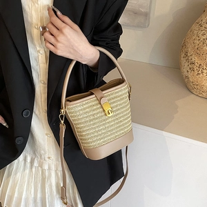 Beige woven straw bucket bag with leather handle and golden clasp shown on a model