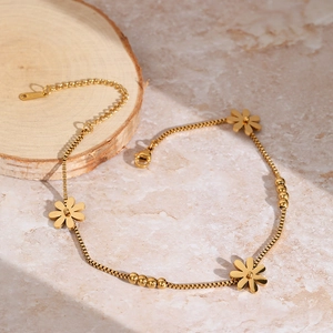 Elegant gold stainless steel daisy anklet with small beads on a marble and wood surface