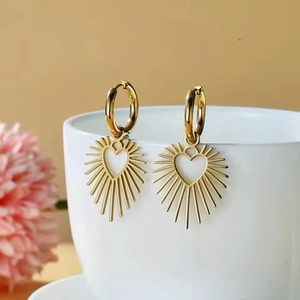 Detailed view of gold hoop earrings with radiant heart pendants on a white cup