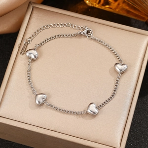 Minimalist silver stainless steel bracelet featuring four heart pendants on a textured box
