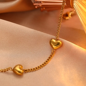 Macro detail of glossy gold heart pendants on a delicate stainless steel chain bracelet