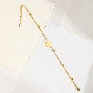 Close-up of golden double heart anklet with engraved letter A and polished beads