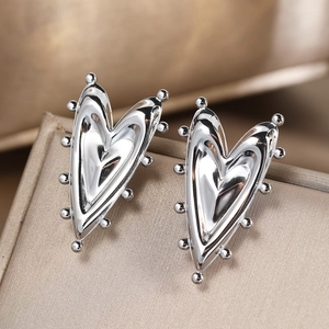 Polished silver heart stud earrings with micro-bead edges on a luxury gift display