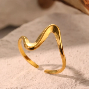 Bague ouverte ondulée minimaliste dorée posée sur une base en pierre rustique
