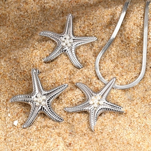 Stainless steel starfish jewelry set with pearls on beach sand background