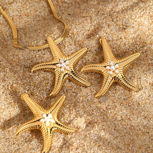 Starfish jewelry set with gold snake chain necklace and pearl earrings on sand background