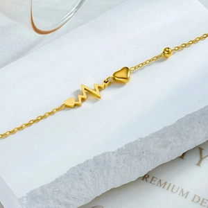 Elegant gold heart and heartbeat charm anklet on white stone display pedestal