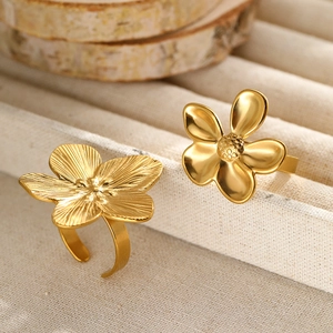 Detail of two gold flower rings with textured and smooth finishes on a rustic display