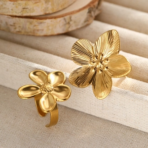 Detail of two gold flower rings with textured petals and adjustable open bands on fabric