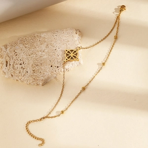Detailansicht eines goldenen zweischichtigen Armbands mit Blumenanhänger und Perlen