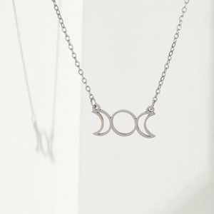 Polished stainless steel triple moon goddess pendant necklace on minimalist white background