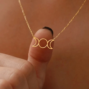 Close-up of golden triple moon pendant necklace on finger showing intricate details