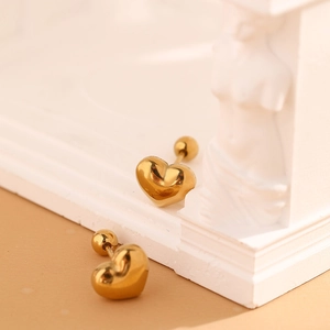 Détail de boucles d'oreilles cœur dorées avec fini miroir devant une statue