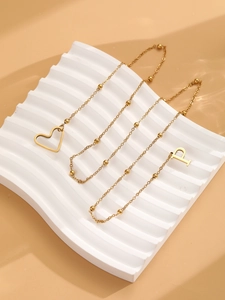 Détail d'un collier en Y doré en acier inoxydable avec pendentifs cœur et lettre P sur perles