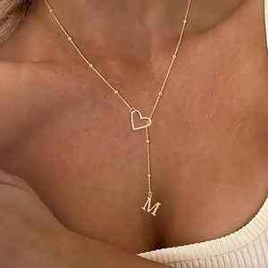 Détail d'un collier en Y doré avec cœur ajouré et pendentif lettre M sur une chaîne perlée