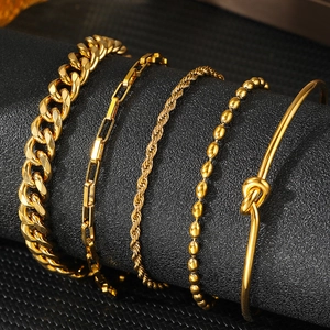 Set of five polished gold bracelets including Cuban and paperclip chains on a display stand