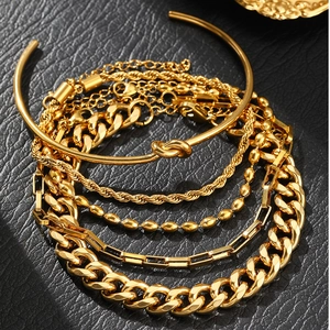 Macro shot of 5-piece gold bracelet set with curb chain, snake chain and cuff on black texture