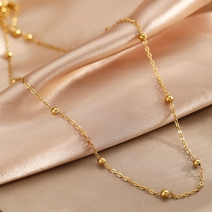 Collier à billes dorées minimaliste pour femme sur tissu en satin champagne