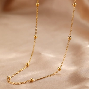 Gros plan d'un collier à billes dorées minimaliste sur un fond de soie couleur champagne