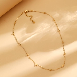 Détail d'un collier chaîne à billes dorées avec fermoir sur fond à ondulations