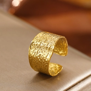 Macro shot of gold-plated wide C-shape ring with unique hammered lava texture on satin