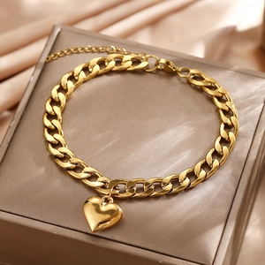 Detail of gold Cuban link anklet with heart pendant on champagne silk background