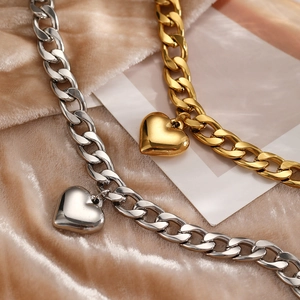 Detail of high-polished gold and silver heart pendants on chunky Cuban chain anklets