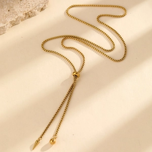 Detailed macro view of adjustable golden box chain with conical pendant on sandstone