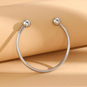 Minimalist stainless steel open bangle featuring polished sphere ends on a beige background