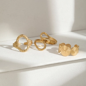 Detailed close-up of three gold stainless steel geometric rings on a white pedestal