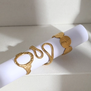 Three gold-plated stainless steel irregular geometric rings on a white display stand