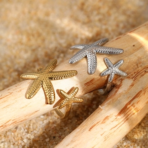 Close-up of gold and silver starfish open rings on a wooden branch over beach sand