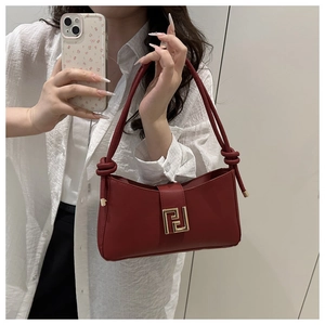 Detail of burgundy shoulder bag featuring a gold geometric buckle and knotted strap