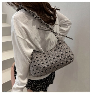 Detailed side view of black and white checkered shoulder bag with bow prints and pleated strap