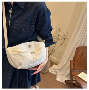 Detail of cream-colored pleated nylon crossbody bag with metal logo and triangular zipper