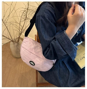 Detail view of a light purple crescent bag with adjustable black strap on navy dress