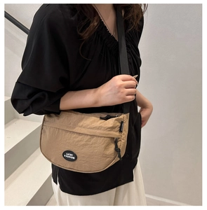 Detail of khaki nylon crescent bag featuring adjustable black strap and front zip pocket