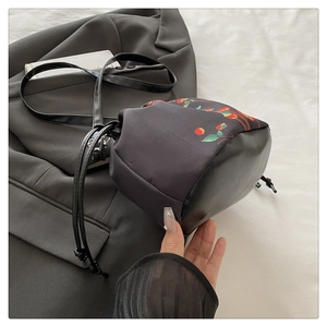 Détail du sac seau à cordon avec imprimé cerises sur un tissu synthétique noir élégant