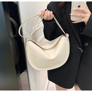 Detail of the minimalist cream-white leather crescent bag on a model's shoulder