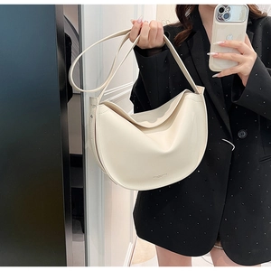 Detail view of a cream leather crescent crossbody bag styled with a black beaded jacket