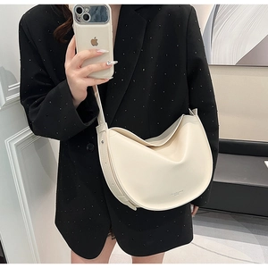 Detail of cream half-moon tote bag with brand logo and adjustable strap worn by model