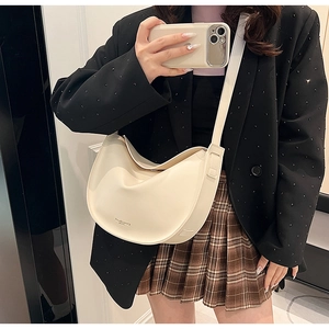 Close-up of cream leather crescent bag with gold logo on casual commuter outfit