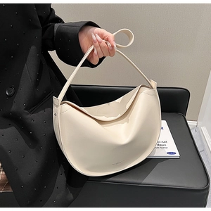 Close-up of a minimalist cream crescent tote bag with smooth leather texture and small logo