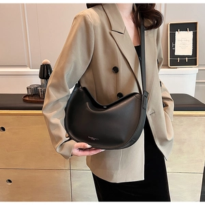Close-up of black crescent bag with silver logo worn by model in a blazer